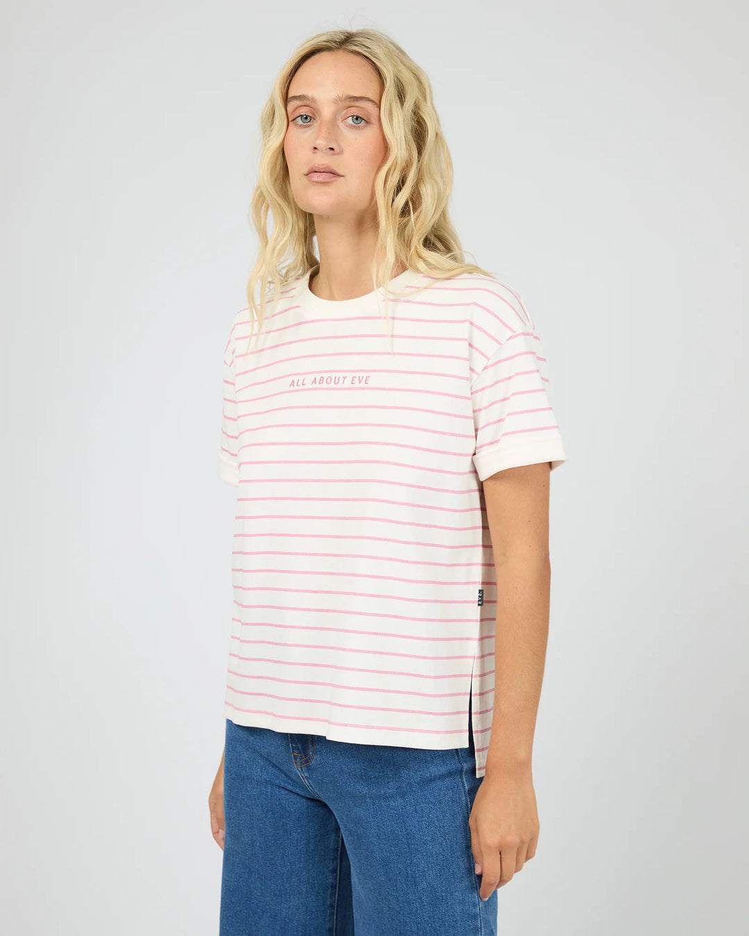 A blonde woman wearing a white short-sleeve t-shirt with thin pink horizontal stripes and &