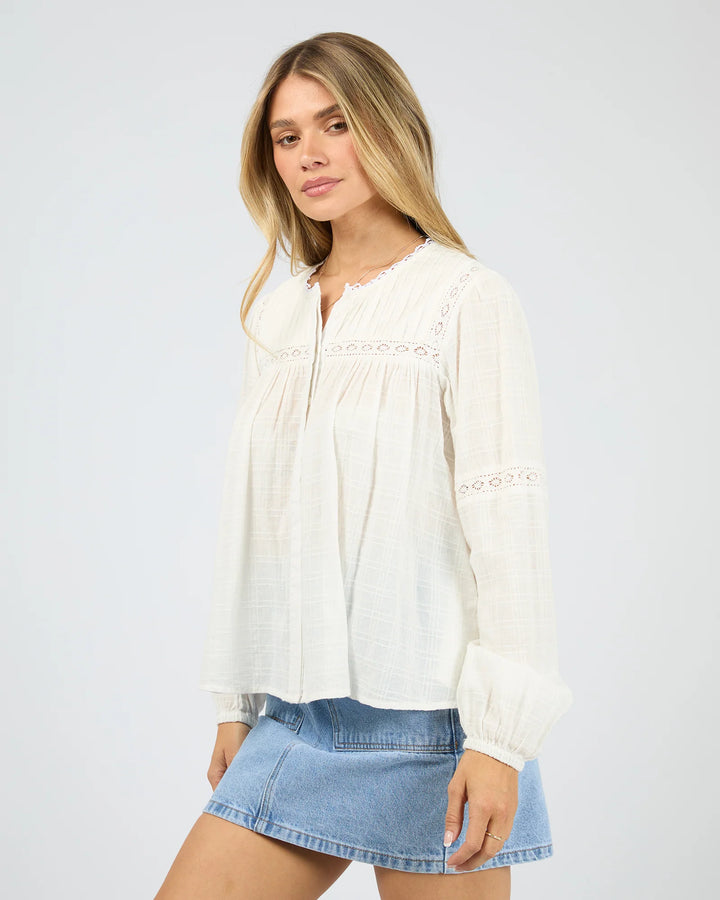 Woman wearing a white blouse with lace details and a denim skirt on a plain background