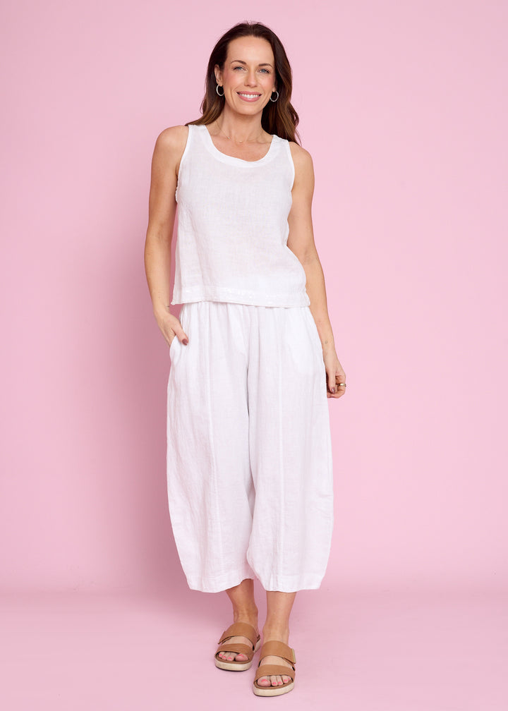 A woman modeling a white sleeveless top and matching white wide-leg cropped pants against a solid pink studio background.