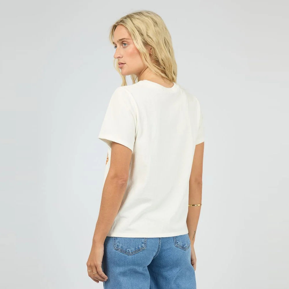 A woman with blonde hair is shown from the back wearing a short-sleeve cream-colored t-shirt and blue jeans against a light gray studio background.