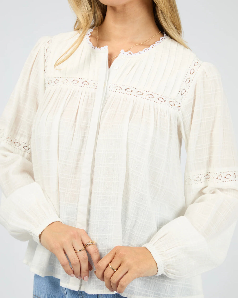 White blouse with lace details worn by a person on a plain background