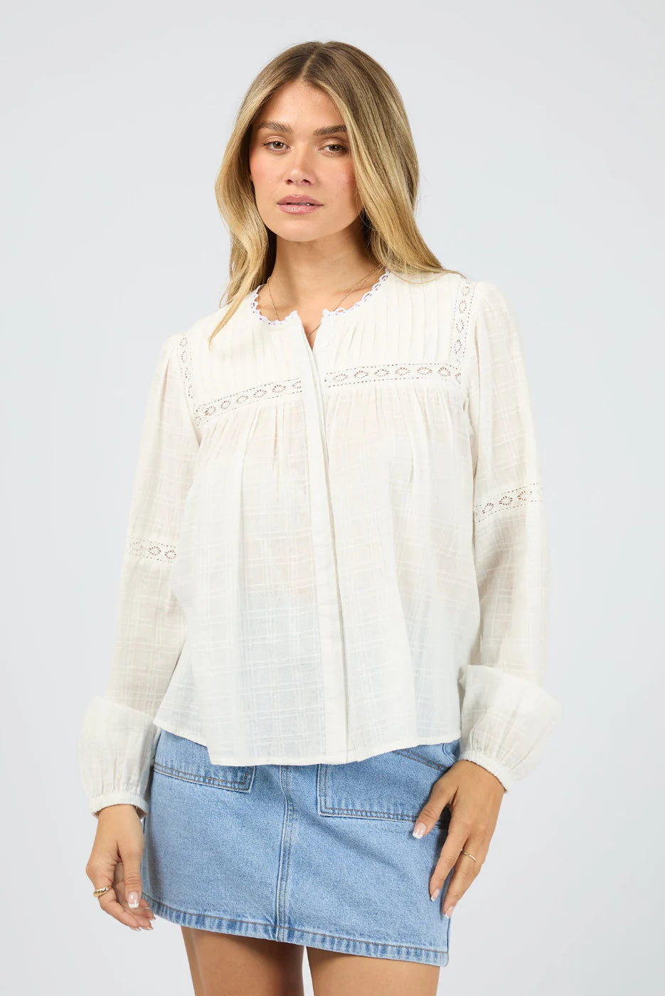 Woman wearing a white blouse and denim skirt on a plain background