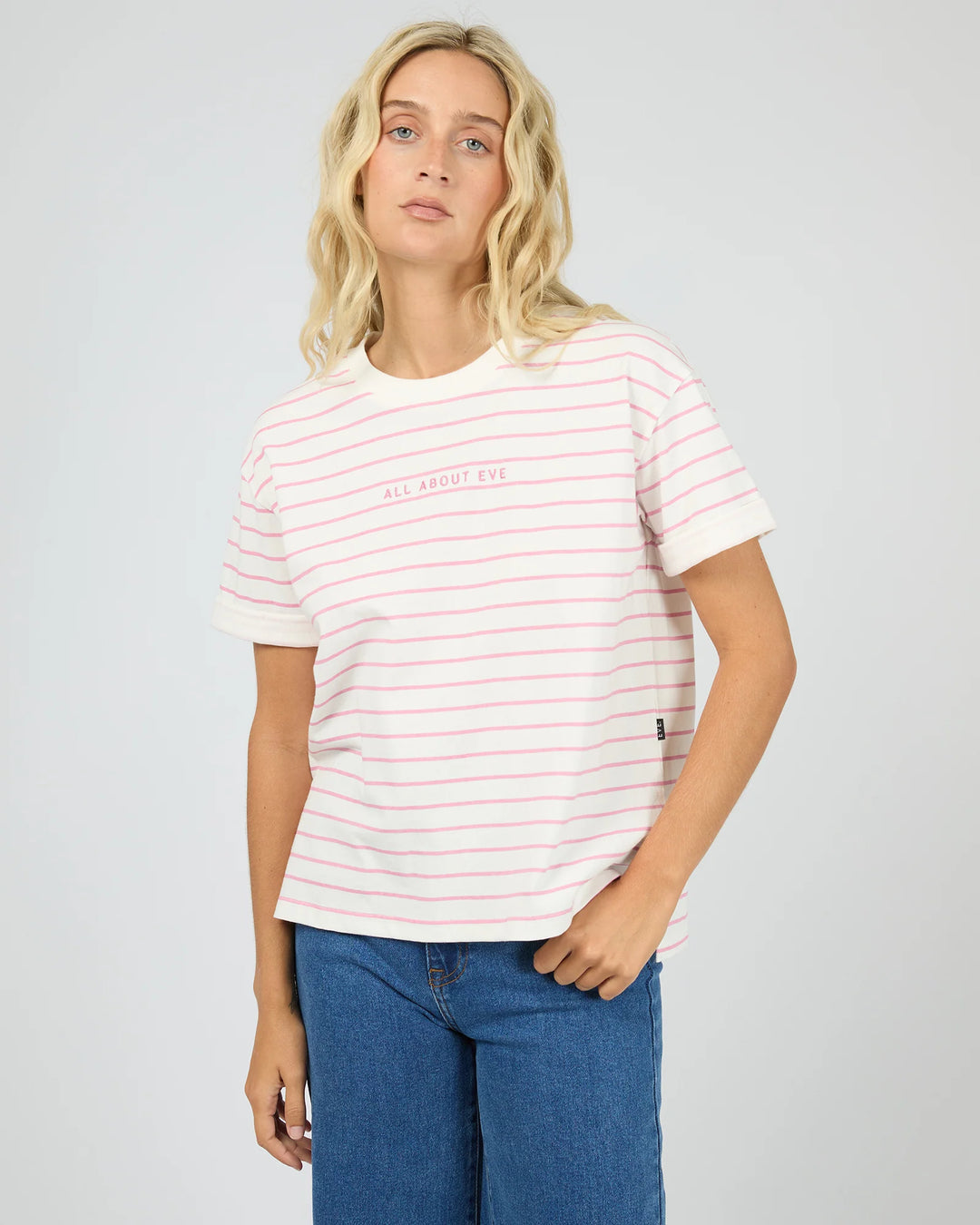 A blonde woman wearing a white short-sleeve crewneck t-shirt with thin pink horizontal stripes and &