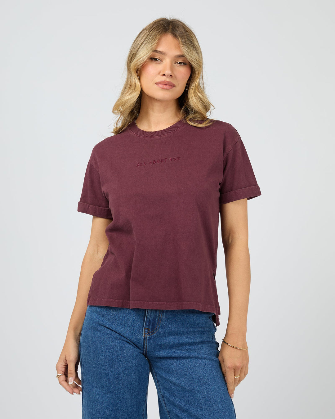 Woman wearing a maroon t-shirt and blue jeans on a light gray background