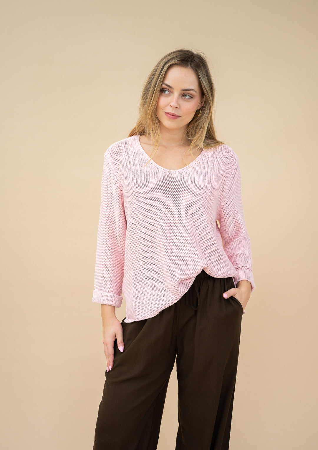 Woman wearing a pink sweater and black pants against a beige background