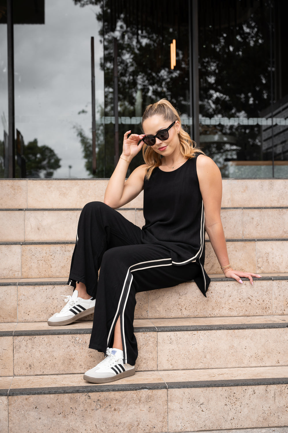 Woman in black tracksuit with white stripes sitting on steps outdoors