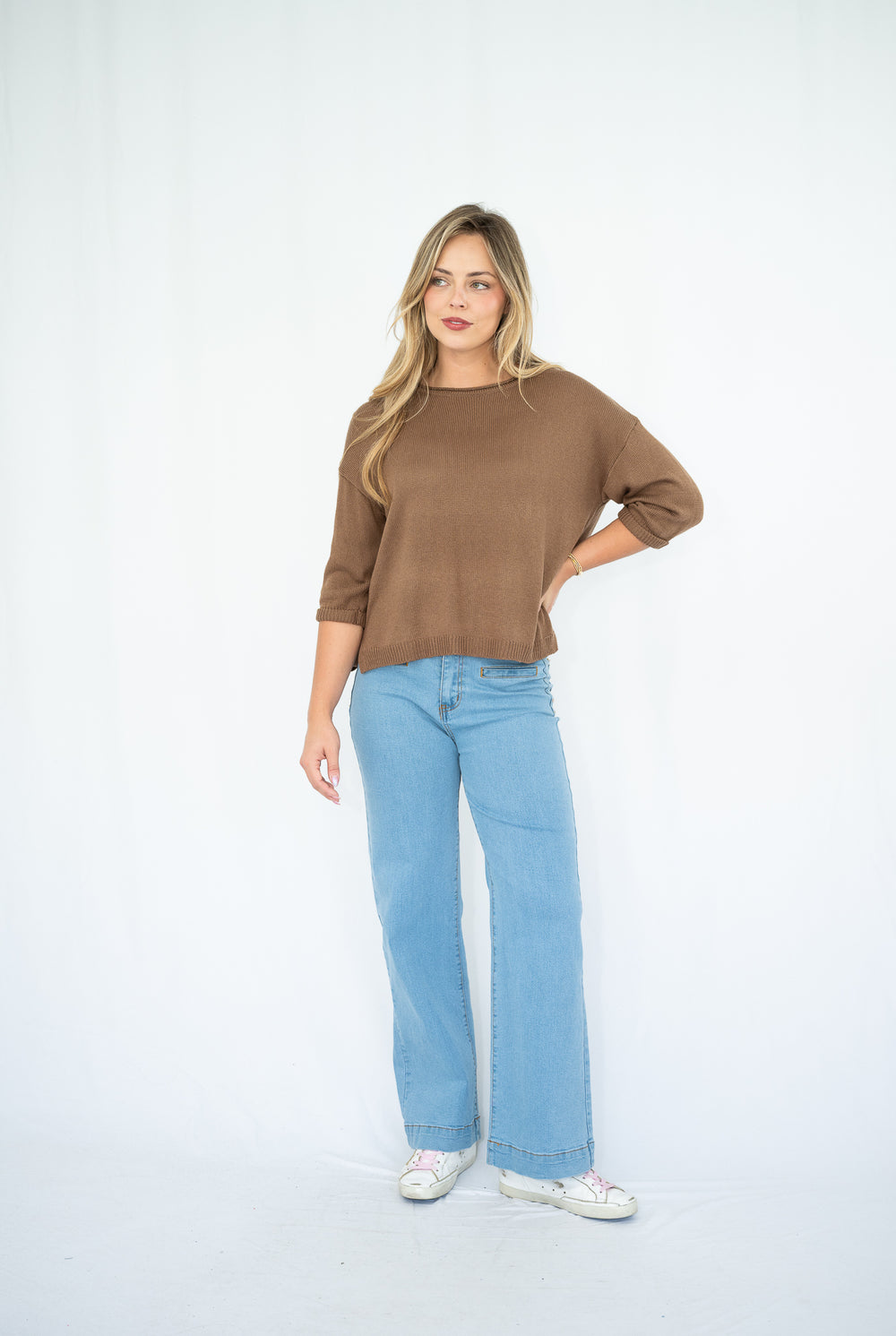 Woman wearing a brown sweater and light blue jeans on a white background