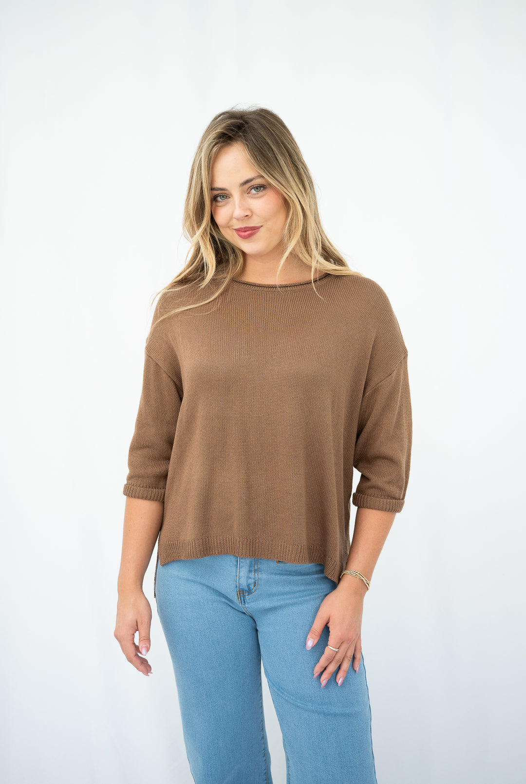 Woman wearing a brown sweater and blue jeans on a white background