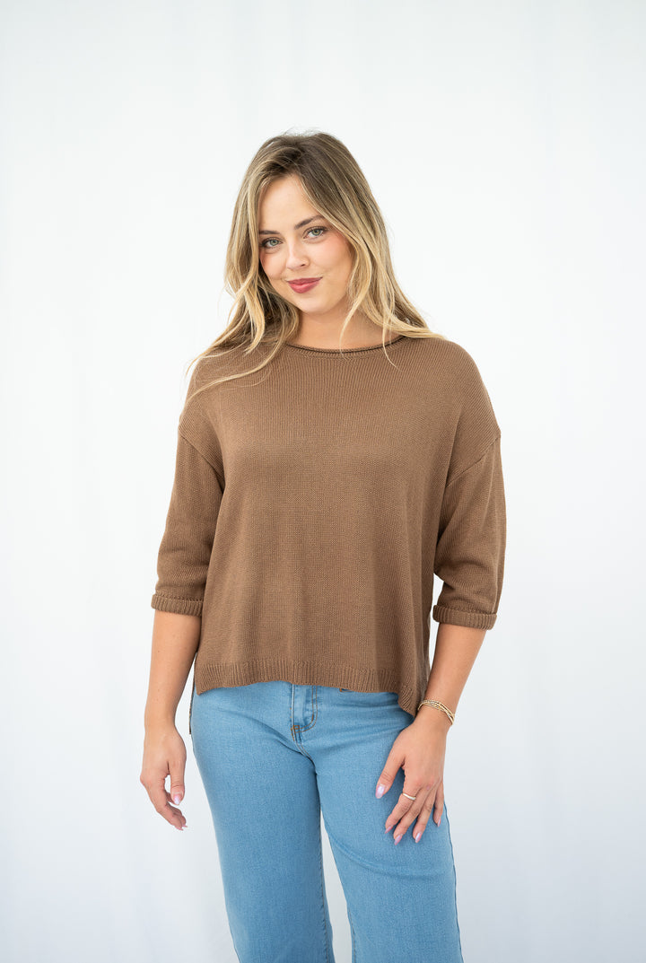 Woman wearing a brown sweater and blue jeans on a white background