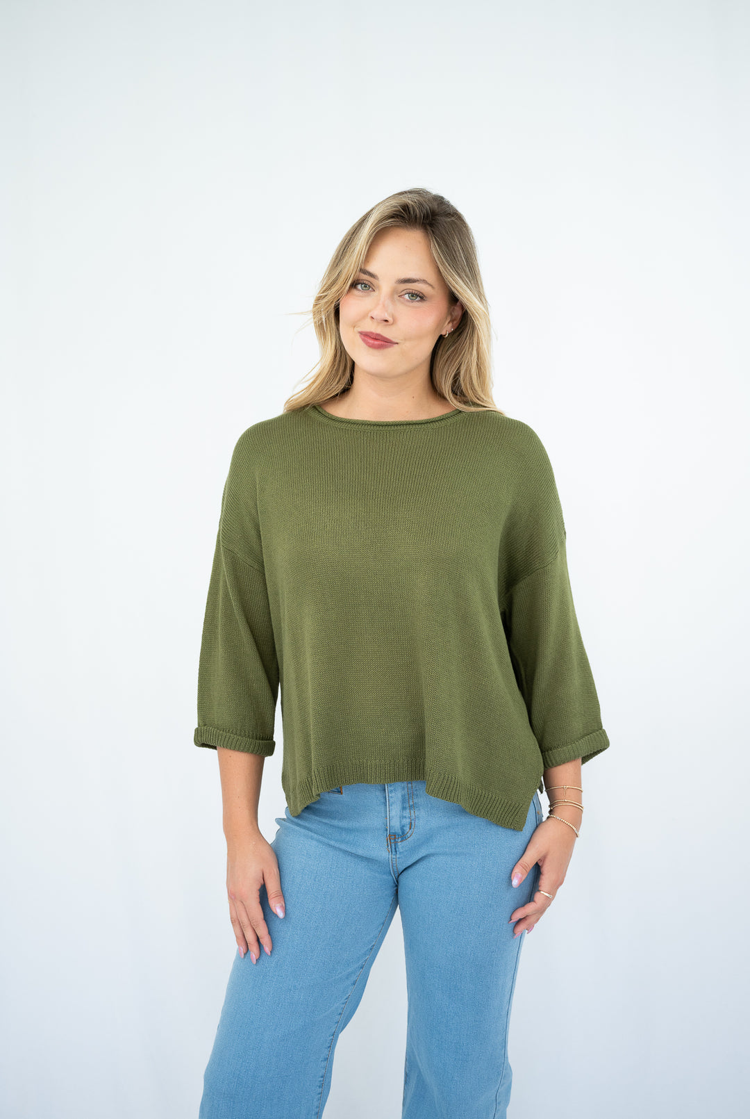 Woman wearing an olive green top and blue jeans on a white background