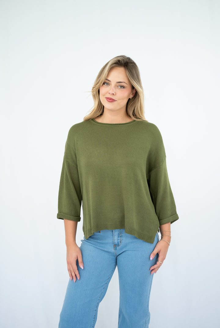 Woman wearing an olive green top and blue jeans on a white background