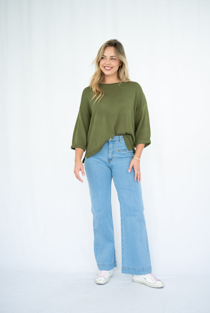 Woman wearing an olive green sweater and light blue jeans on a white background