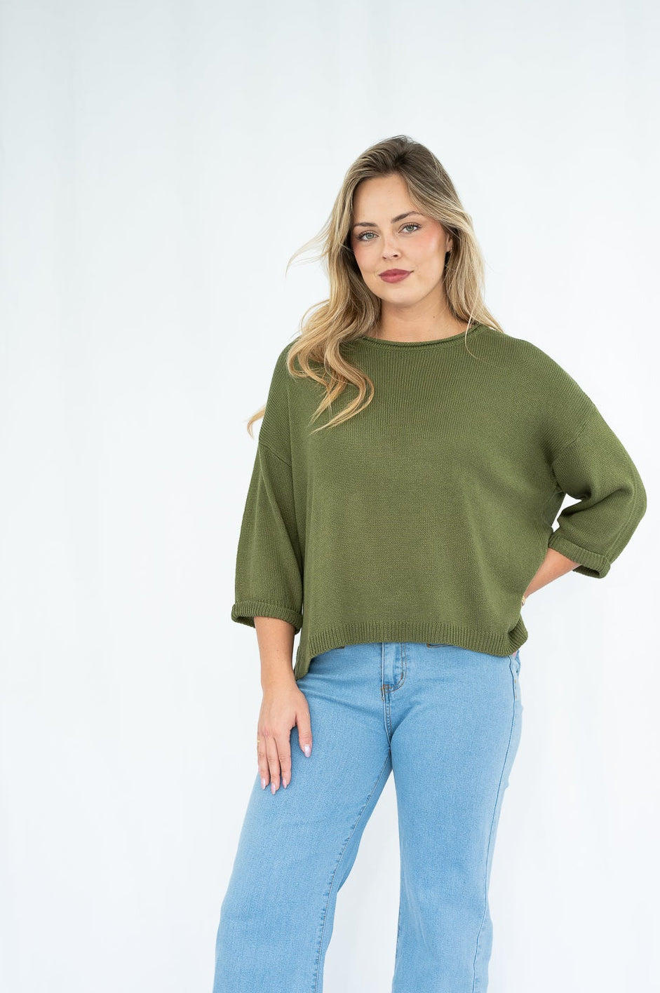 Woman wearing a green sweater and blue jeans on a white background