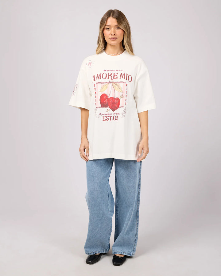 Person wearing a white t-shirt with graphics and text, paired with blue jeans on a plain background