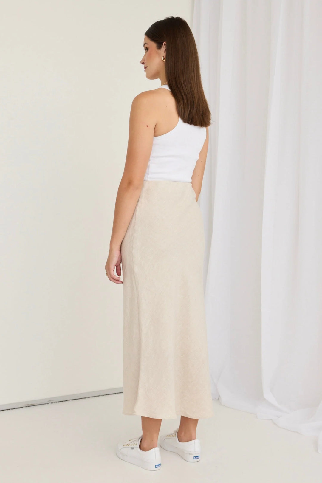 Woman wearing a white top and beige skirt against a white curtain background