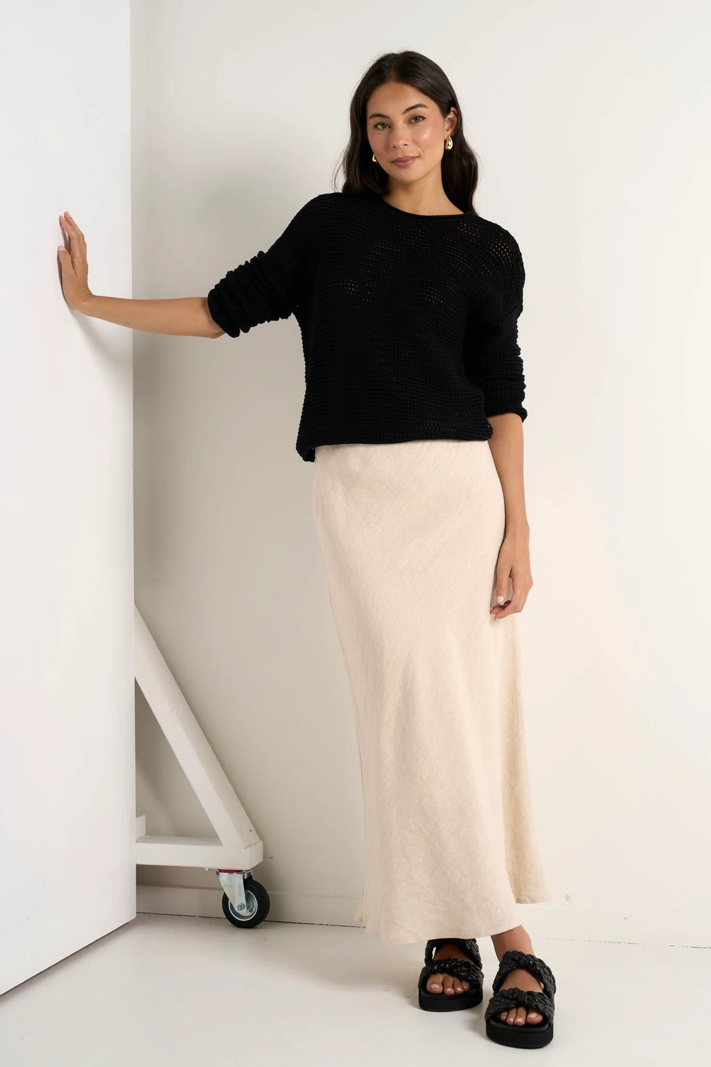 A woman standing in a room wearing a beige natural linen skirt with a black top.