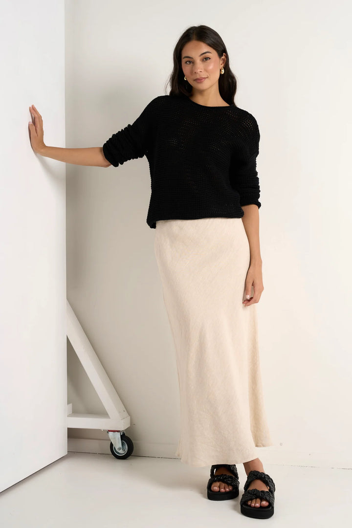 A woman standing in a room wearing a beige natural linen skirt with a black top.