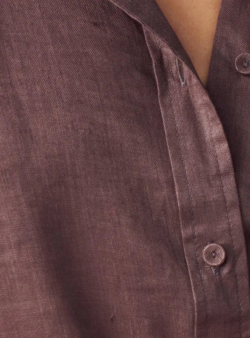 Close-up of a textured button-up shirt in a muted dusty mauve-brown color, showing the fabric weave and a button closure.