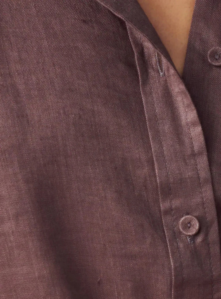 Close-up of a textured button-up shirt in a muted dusty mauve-brown color, showing the fabric weave and a button closure.