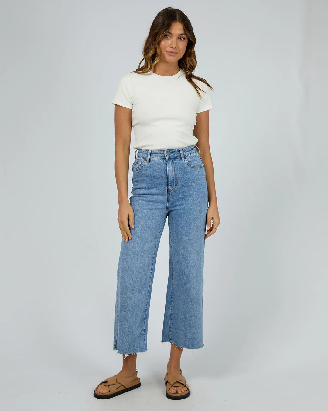 Woman wearing a white t-shirt and blue jeans on a plain background
