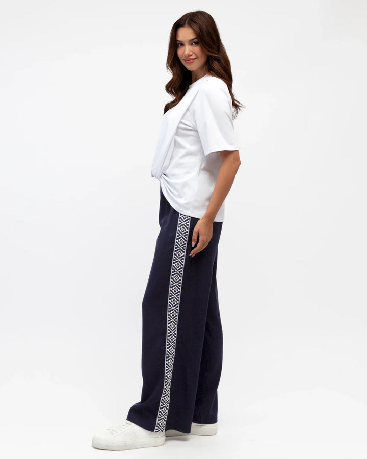 Woman wearing a white top and navy pants with a patterned side stripe on a white background