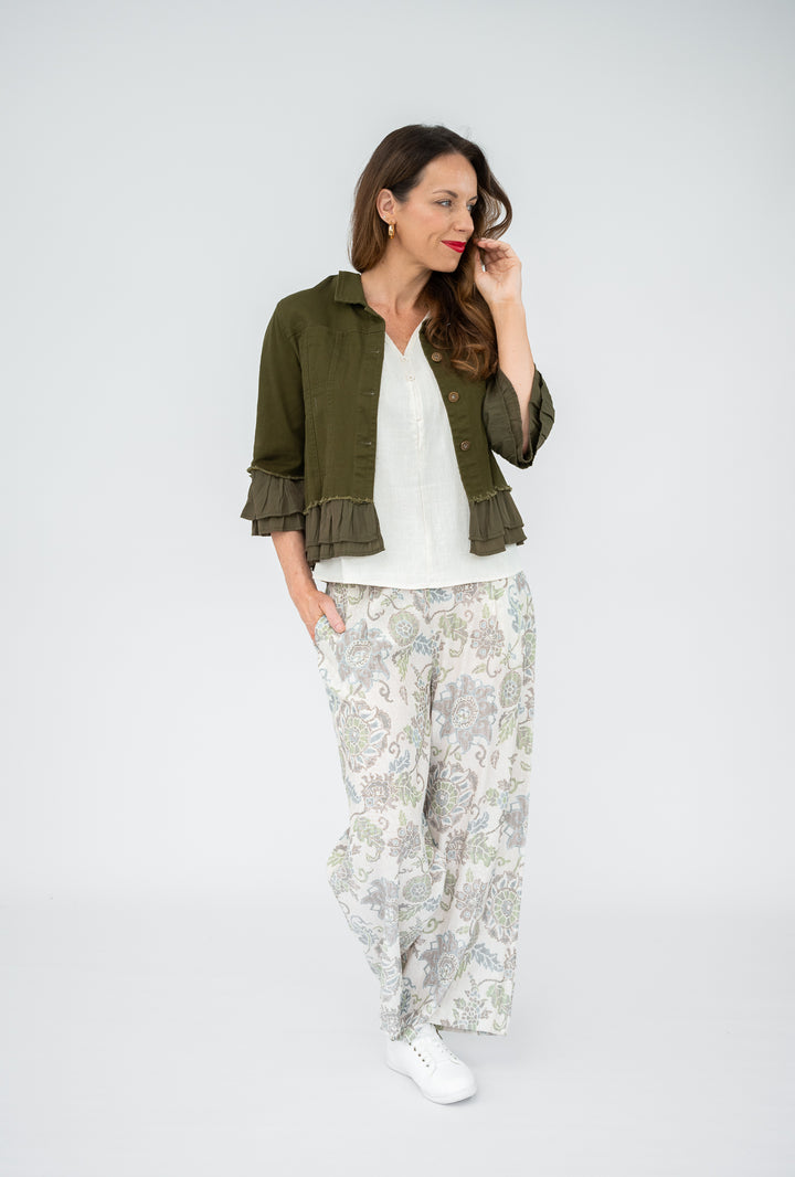 Woman wearing a green jacket, white top, and floral pants on a white background