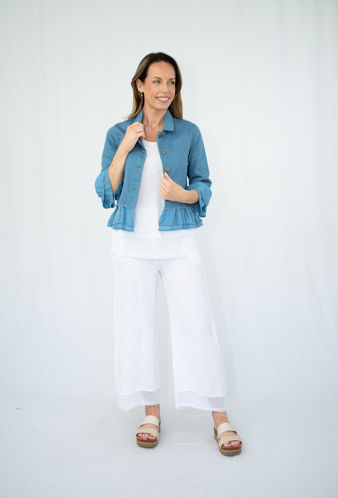 Woman wearing a blue denim jacket over a white top and pants on a white background