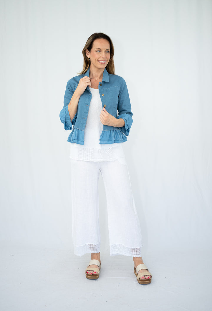 Woman wearing a blue denim jacket over a white top and pants on a white background