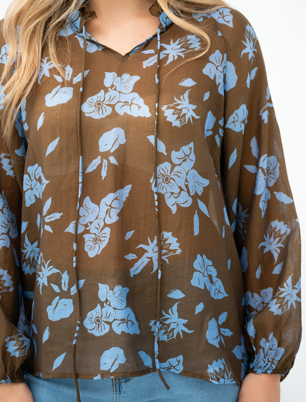 Woman wearing a brown floral blouse with blue pants on a white background