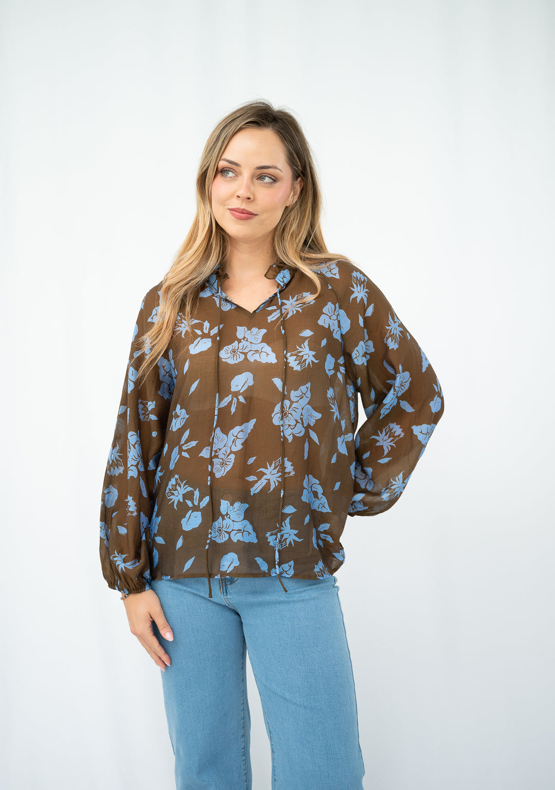 Woman wearing a brown floral blouse with blue pants on a white background