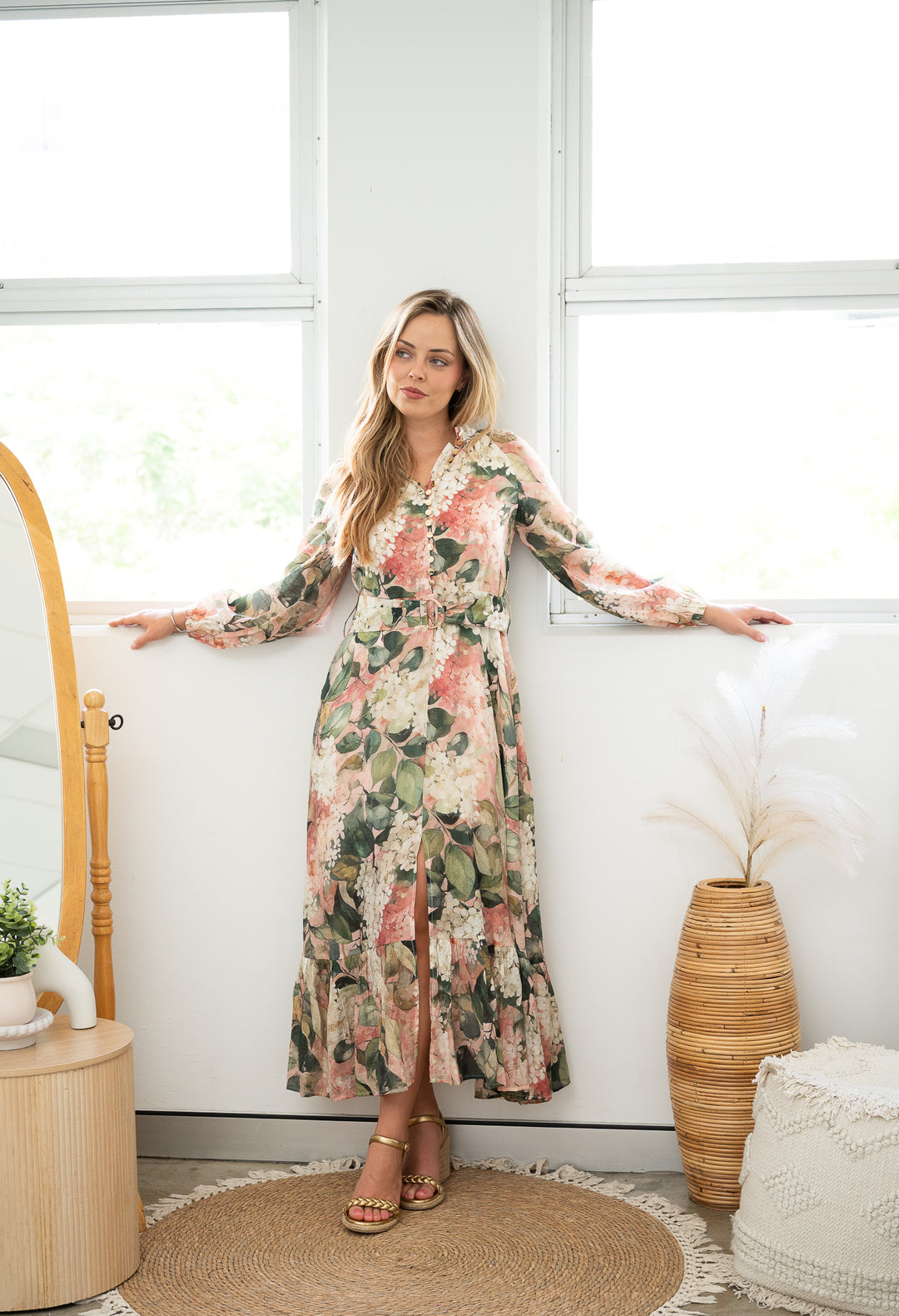 Woman in a floral dress standing in a bright room with white walls and decorative elements.