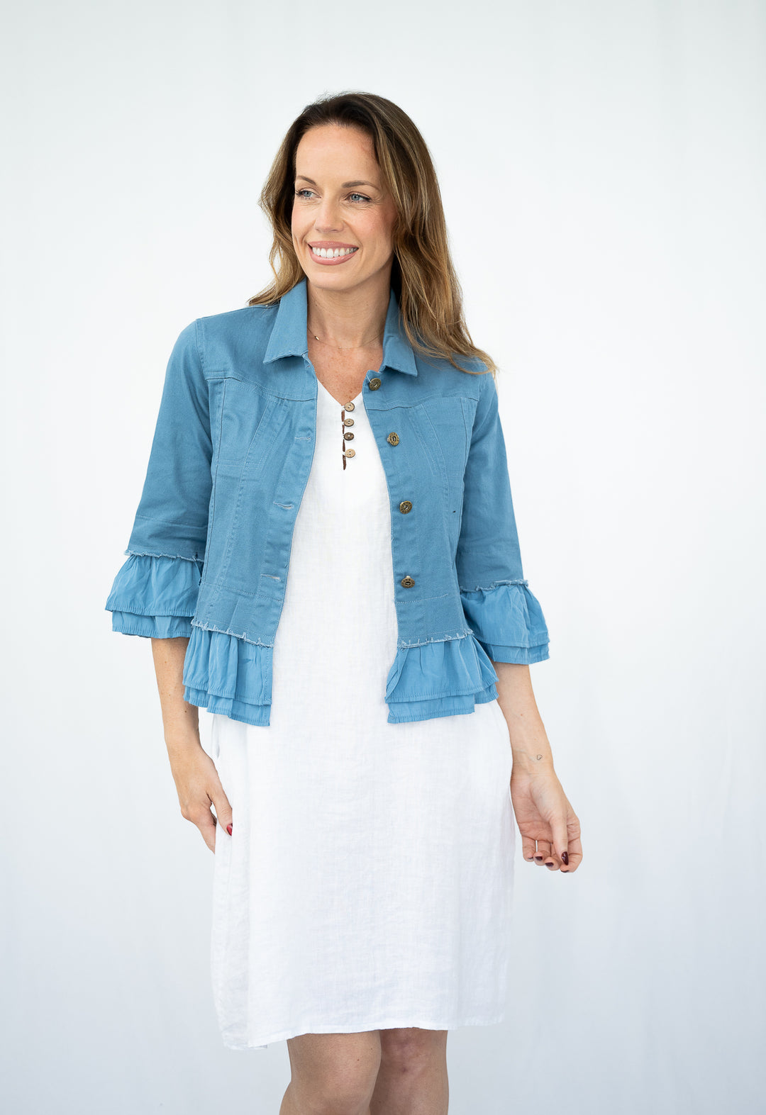 Woman wearing a blue denim jacket over a white dress on a white background