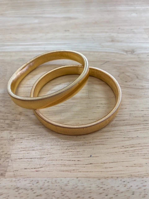 A pair of gold elastic sleeve keepers placed on a wooden surface.