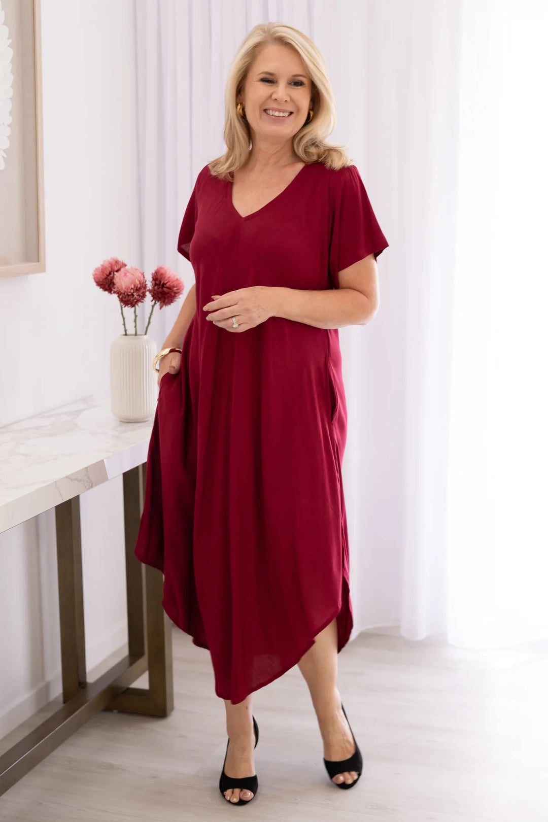 Woman wearing a burgundy dress in a bright room with white curtains.