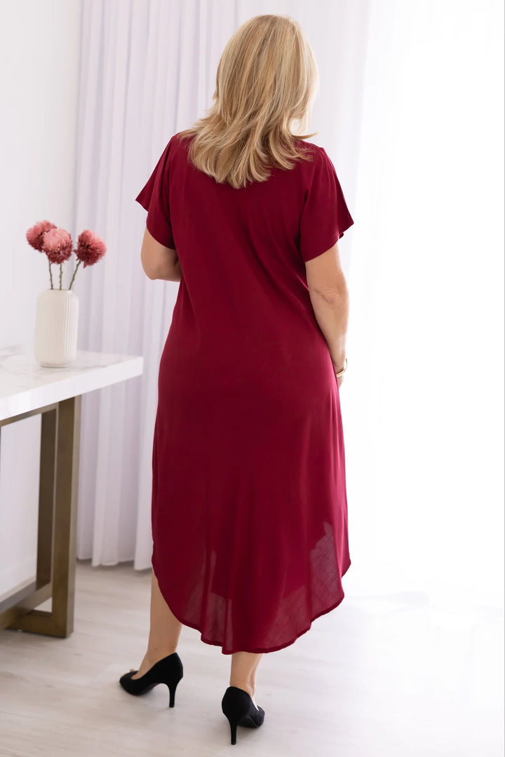Woman wearing a red dress standing in a room with a table and flowers.