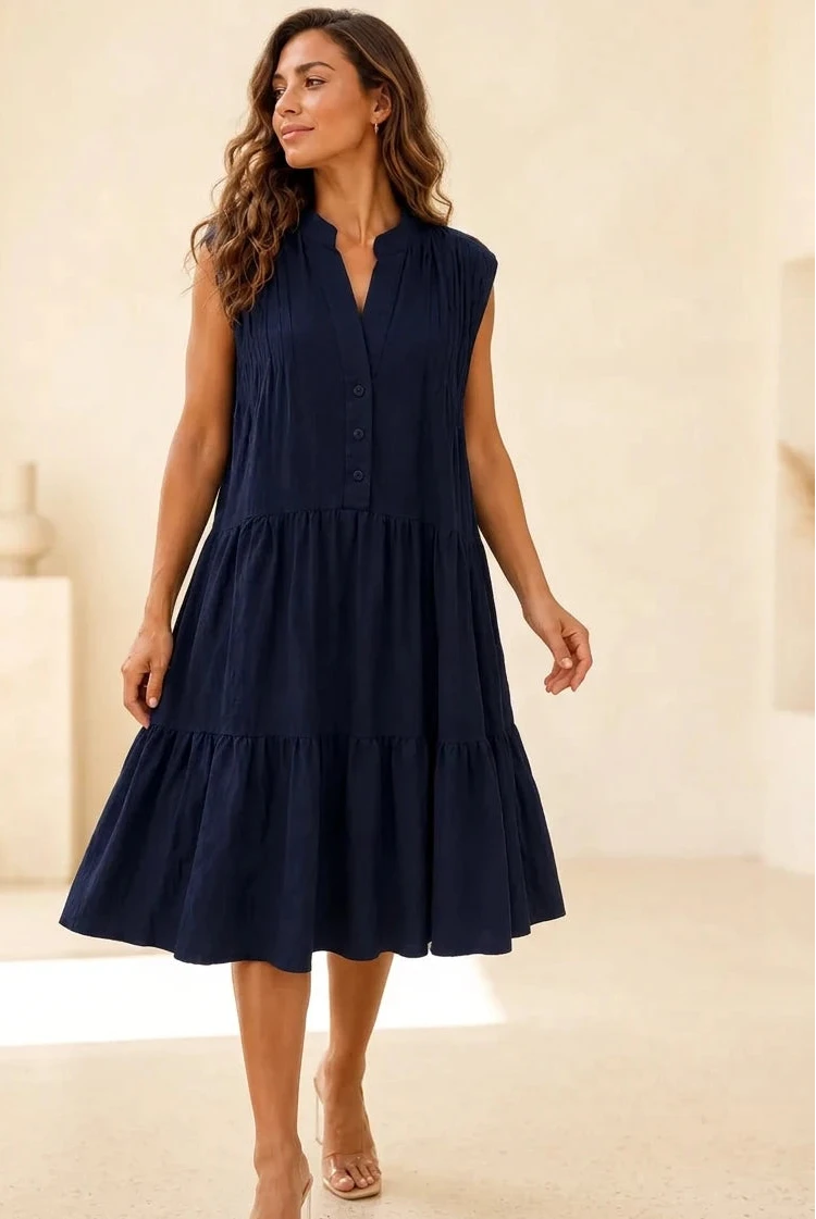 A woman wearing a sleeveless navy blue tiered midi dress with a buttoned V-neckline