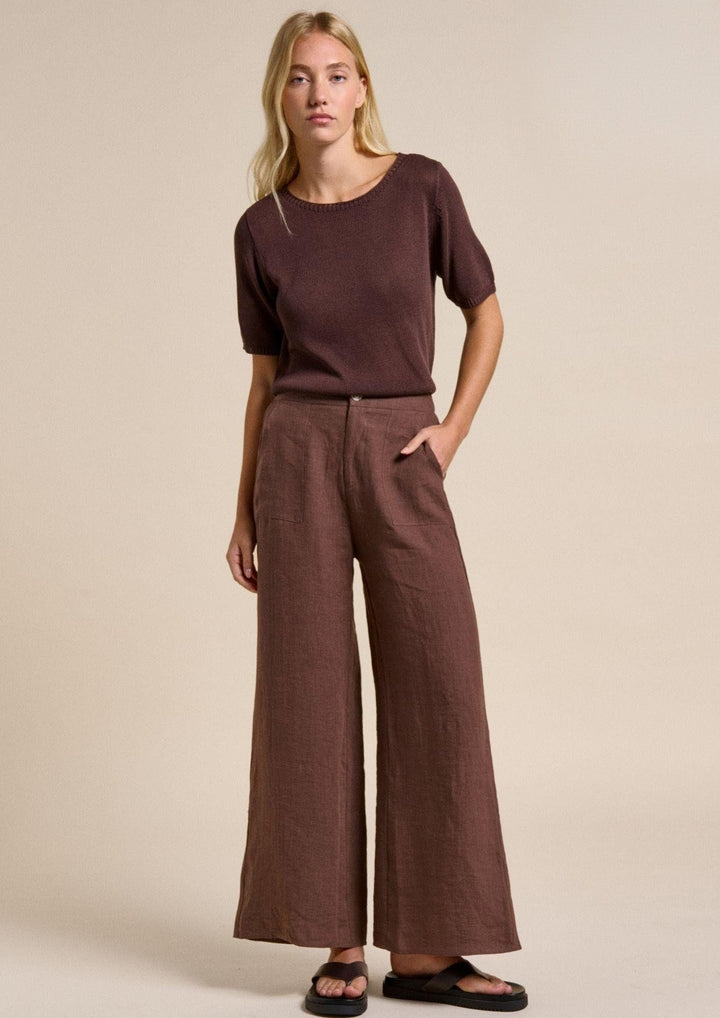 Woman wearing a brown outfit with wide-leg pants on a beige background