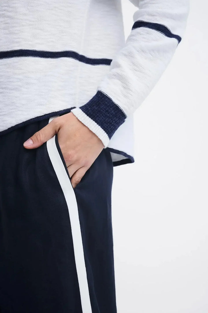 Close-up of a person wearing a white and navy striped long-sleeve top with navy and white striped cuffs, paired with dark navy pants featuring a white side stripe, with the hand in the pocket.