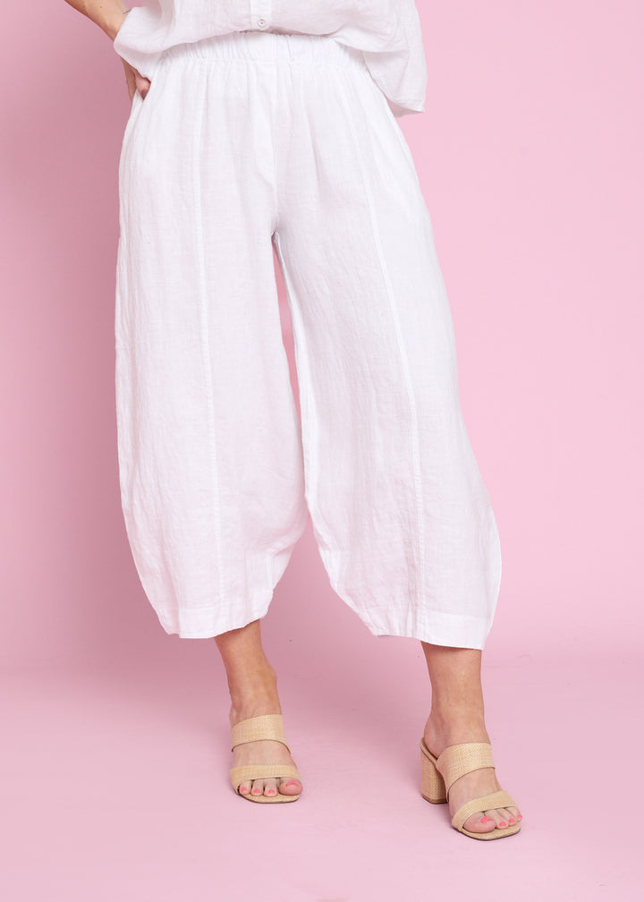 White wide-leg cropped pants with a high waist, modeled with beige heeled sandals against a solid pink background.