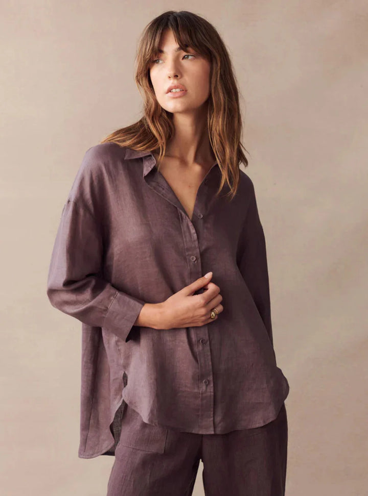 Woman wearing a loose-fitting, long-sleeve purple shirt and pants against a beige background