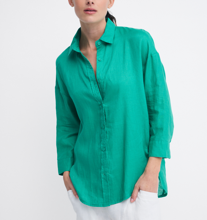 A woman wearing a bright green linen button-up shirt with white pants, photographed against a clean white studio background.