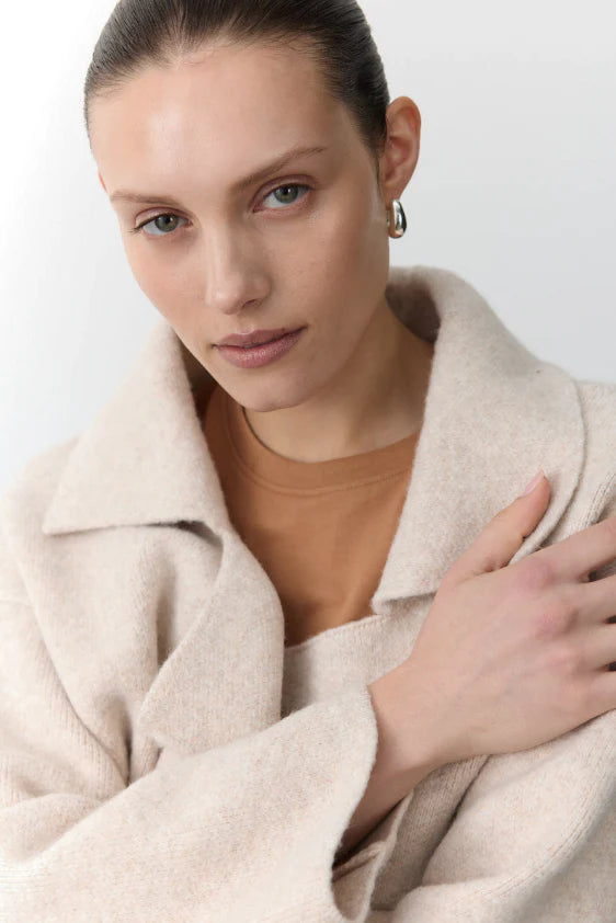 Woman wearing a beige coat over a brown top against a white background