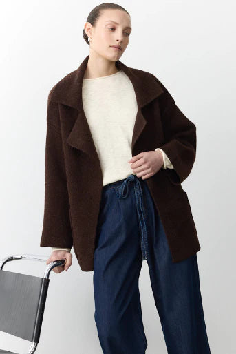Woman wearing a brown coat over a white sweater and blue jeans, holding a black chair.