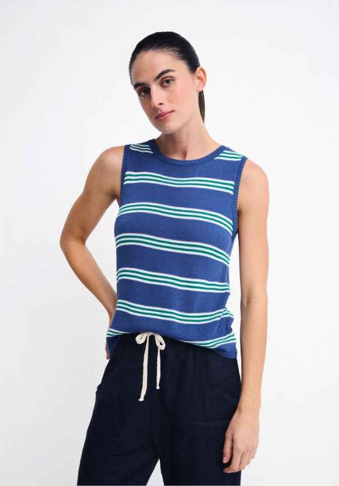 A woman modeling a sleeveless knit top with horizontal navy, light blue, and mint green stripes, paired with dark navy drawstring pants, against a plain light gray studio background.