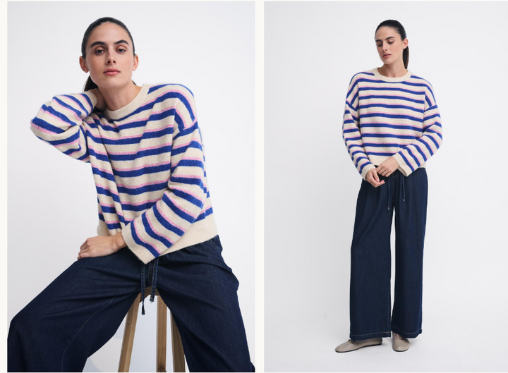 A model wearing a blue and cream striped knit sweater and dark wide-leg pants, shown in two studio poses against a light gray background.