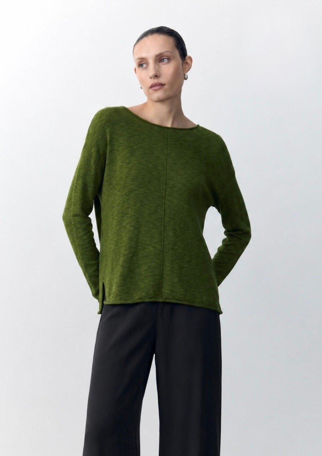 Woman wearing a green sweater and black pants on a white background