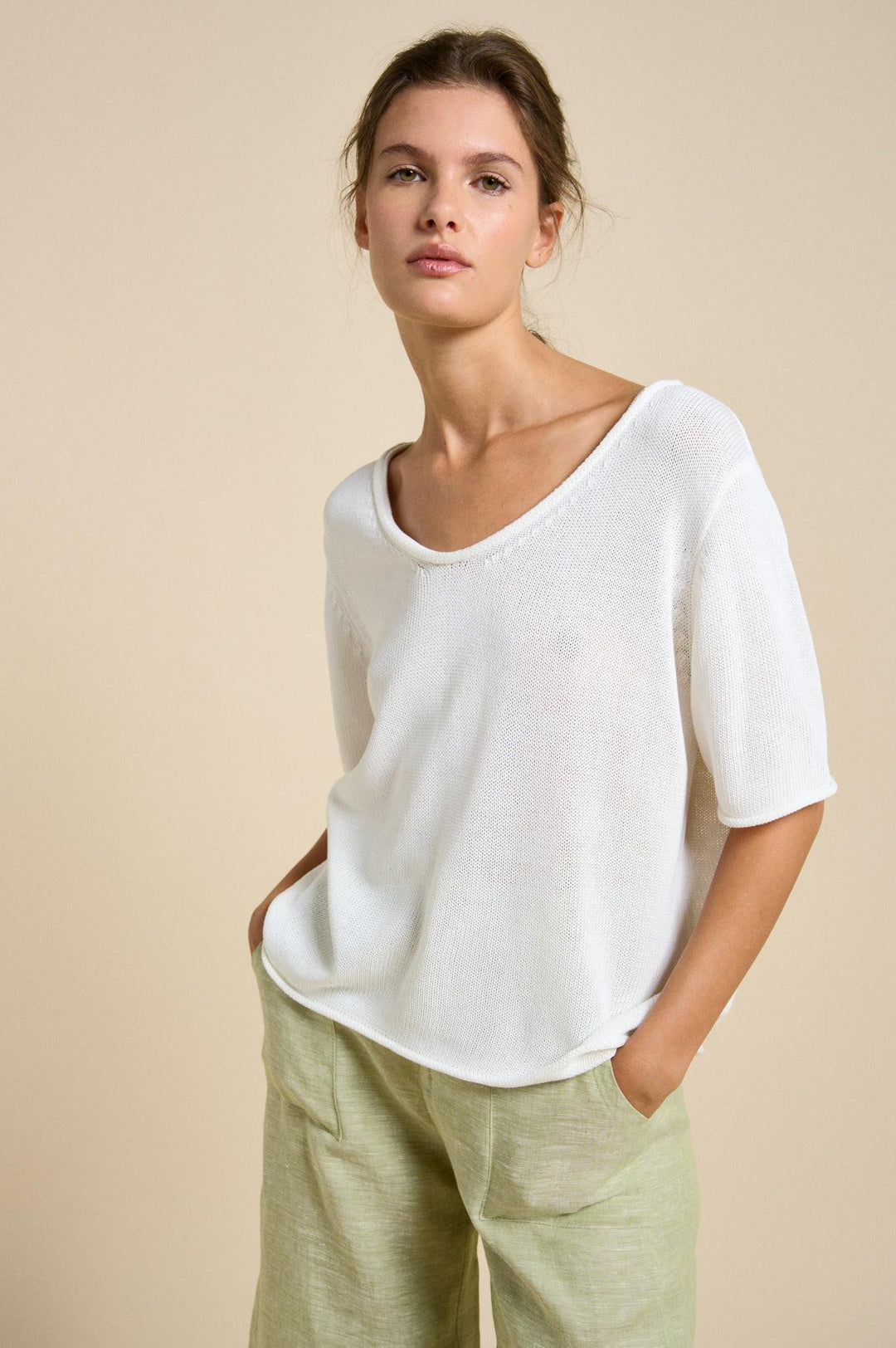 Woman wearing a white top and green pants against a beige background