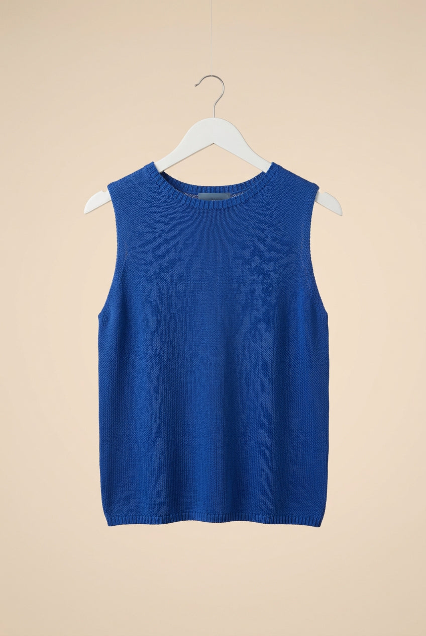 A sleeveless blue knit top hanging on a white hanger against a white paneled door.