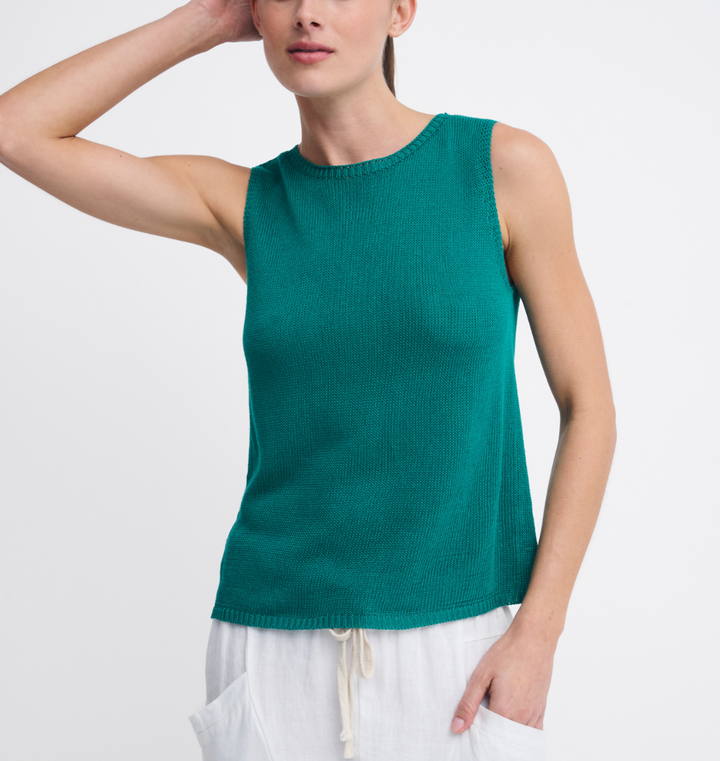 A woman wearing a sleeveless ribbed knit top in a rich teal green color, paired with white drawstring pants, against a clean white background.