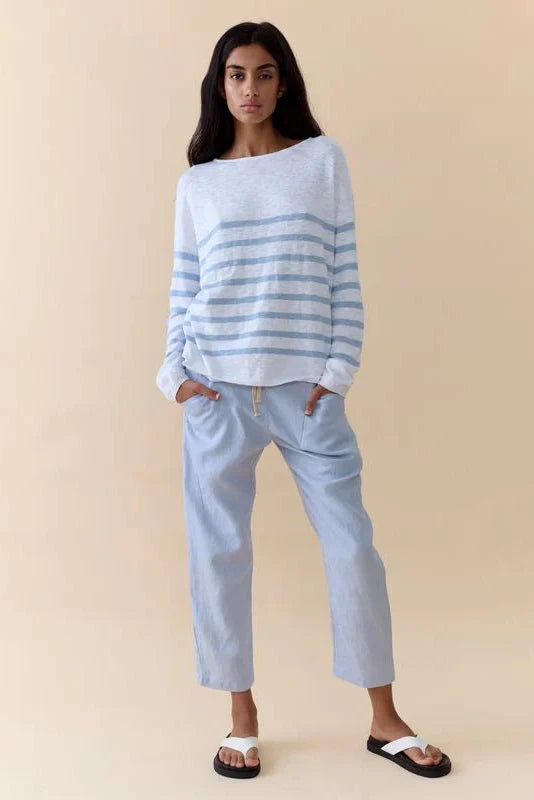 A woman modeling a light blue and white striped knit sweater and matching light blue cropped pants against a solid beige studio background.